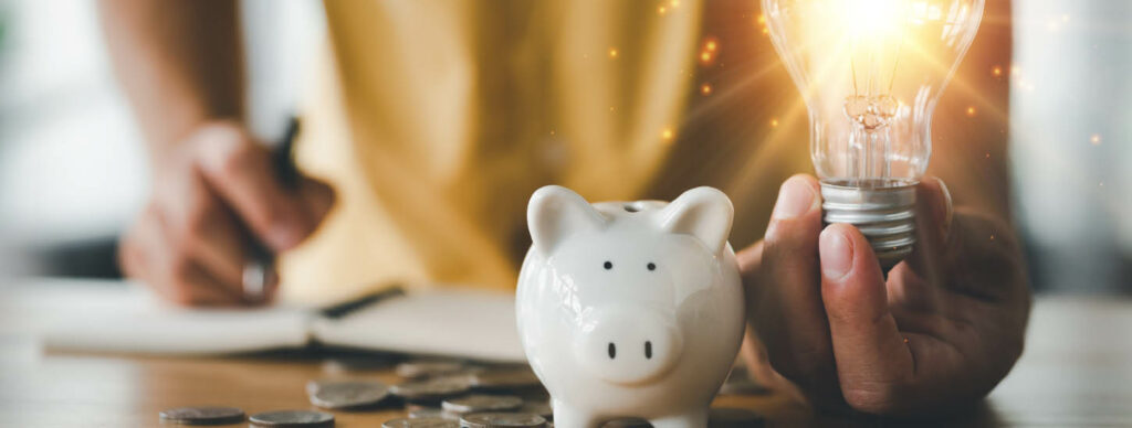 person writing in a notebook with a piggy bank and a bright lightbulb in hand